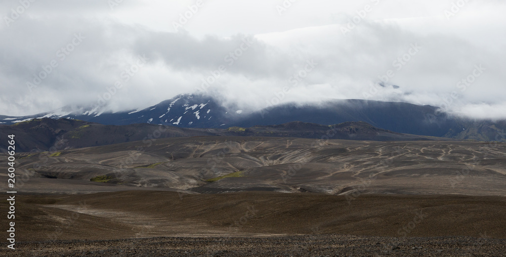 Black lava hills at the foot of the green mountains with snowy hills