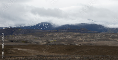 Black lava hills at the foot of the green mountains with snowy hills