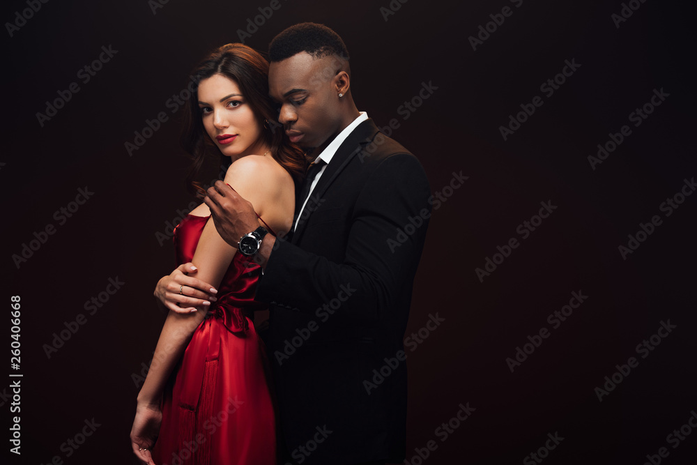 african american man undressing beautiful woman in red dress isolated on black with copy space