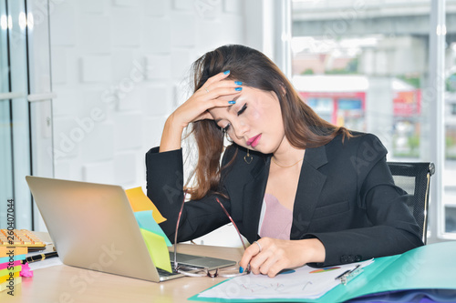 Stressed business woman sitting and holding head because of pain headache in modern office