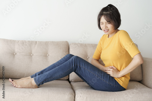 Young asian woman sit on sofa in the living room. she having painful stomachache. © sorrapongs