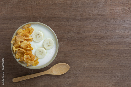 top view of natural yogurt with banana and corn flakes in a ceramic bowl on wooden table. healthy food concept.