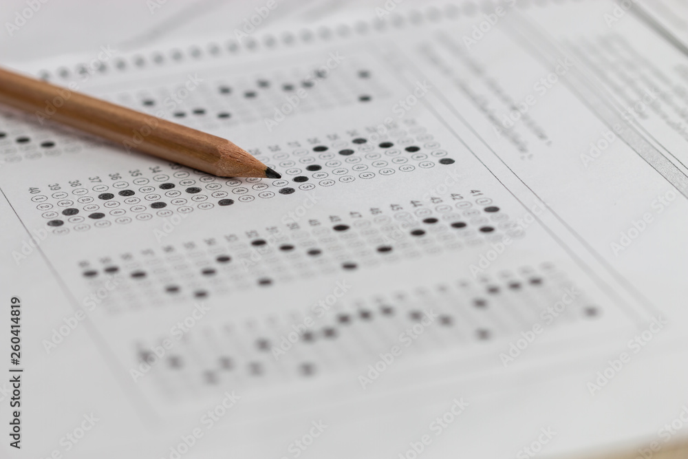Standardized test exam multiple carbon paper form with gray black answers sheet bubbled and pencil resting on university classroom. Examination knowledge in school concept Standardized test exam multiple carbon paper form with gray black answers sheet bubbled and pencil resting on university classroom. Examination knowledge in school concept