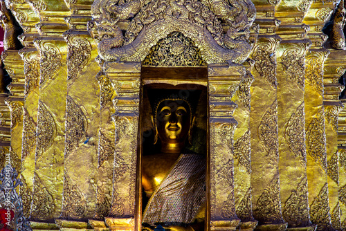 Golden Buddha image in golden pagoda with details of Thai art in a Buddhist temple in Thailand.