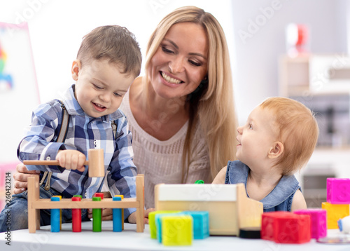 babysitter and children playing together in nursery or day care centre
