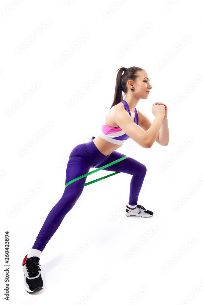 Sporty woman does exercises on legs, makes lunges with sport fitness rubber bands on white background. Photo of muscular woman in sportswear on white background. Strength and motivation. Sporty woman does exercises on legs, makes lunges with sport fitness rubber bands on white background. Photo of muscular woman in sportswear on white background. Strength and motivation.