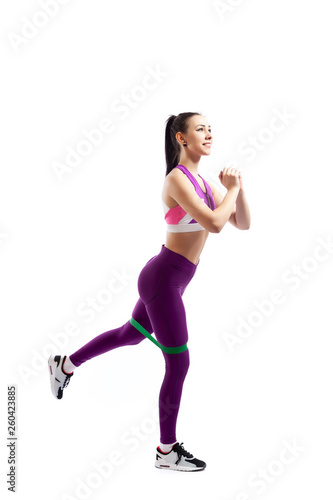 Sporty woman does exercises on legs with sport fitness rubber bands on white background. Photo of muscular woman in sportswear on white background. Strength and motivation.