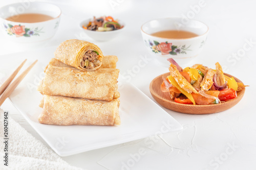 Traditional Chinese tortillas filled - bings in a plate on a white background, salads, Dam Sam snacks and cup of tea.