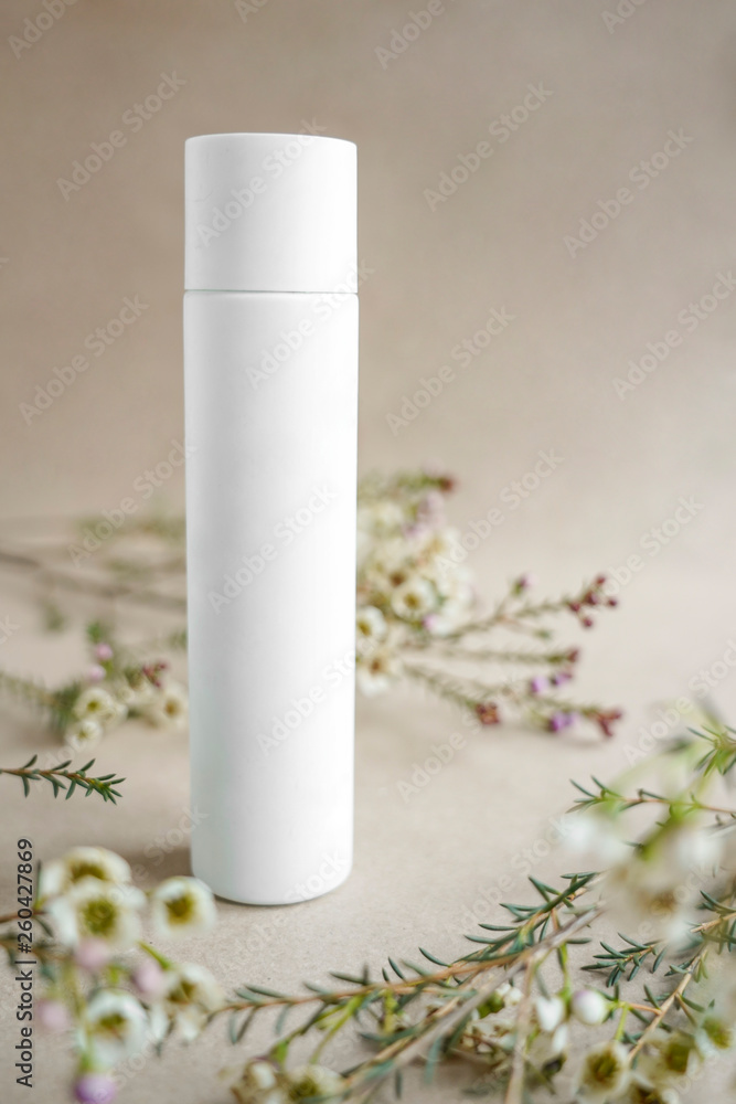 White cosmetic bottle on beige background decorated with white flowers White cosmetic bottle on beige background decorated with white flowers