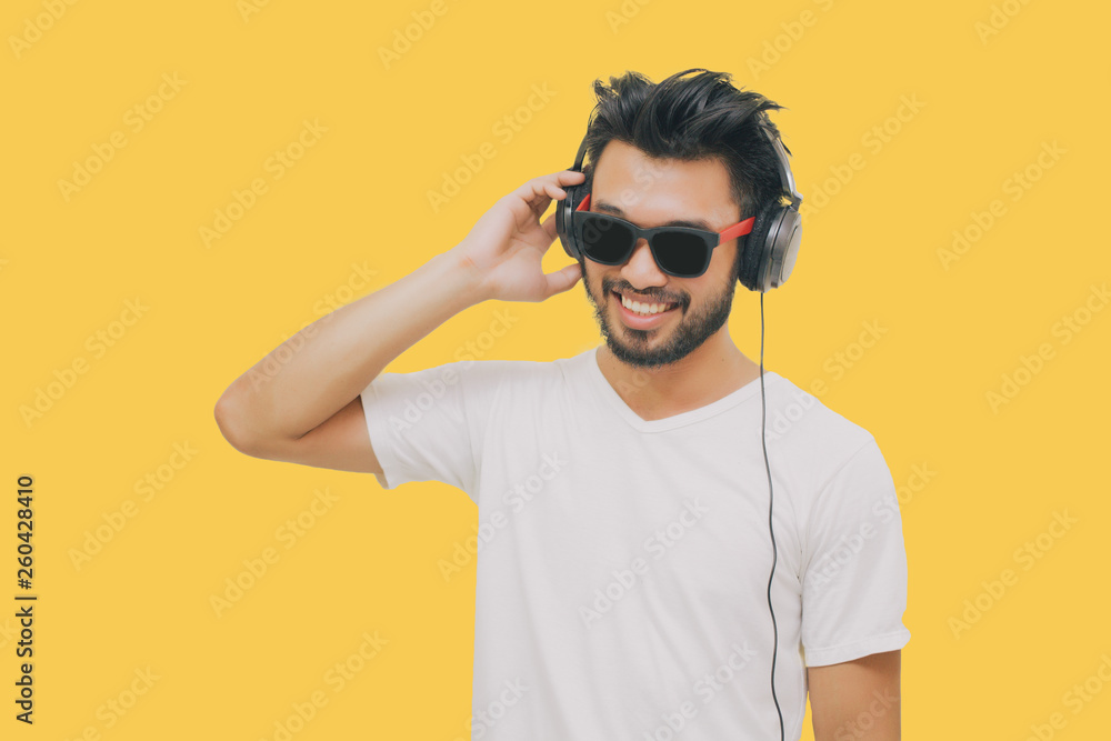 Asian handsome man with a mustache, smiling and laughing and using smart phone to listen music with headphones on yellow background Asian handsome man with a mustache, smiling and laughing and using smart phone to listen music with headphones on yellow background