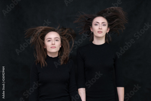 Concept portrait of two stylish brunette sisters on a black background in various poses. Fashionable photo of two beautiful girls with dark hair