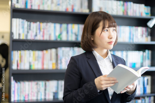 本棚を前に本を読む女性