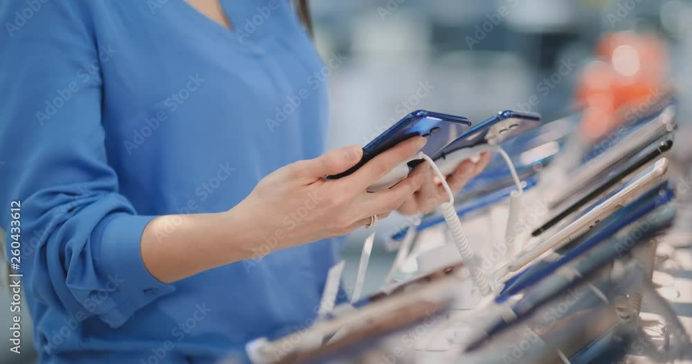 Close-up of a woman holding two new smartphones in her hands and choosing the best phone model in the modern electronics store to buy Close-up of a woman holding two new smartphones in her hands and choosing the best phone model in the modern electronics store to buy