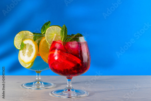 Two refreshing cocktails with orange lemon lime mint and ice on a bright blue background