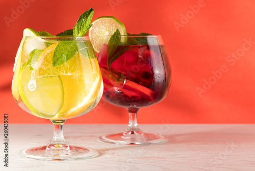 Two refreshing cocktails with orange lemon lime mint and ice on a bright coral background