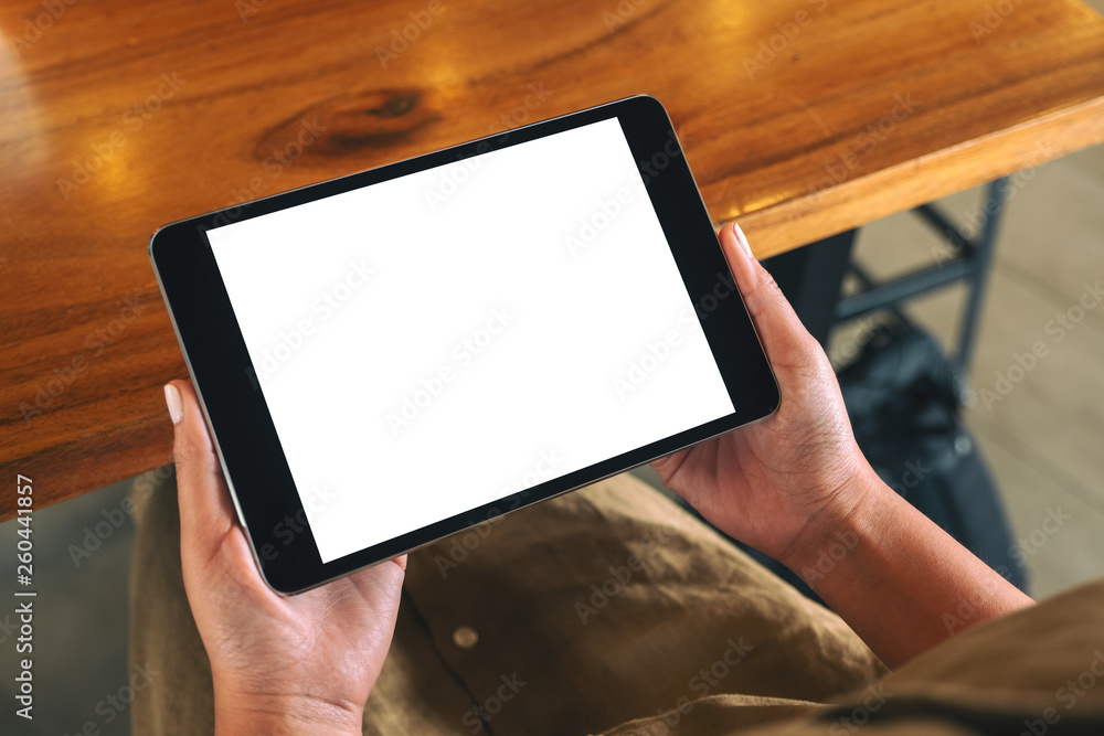 Mockup image of a woman sitting and holding black tablet pc with blank white desktop screen horizontally Mockup image of a woman sitting and holding black tablet pc with blank white desktop screen horizontally