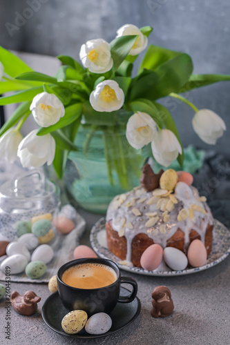 Fragrant cup of coffee and Easter orthodox sweet bread, kulich and colorful quail eggs with willow branches. Holidays breakfast concept with copy space. Set for the holiday and a bouquet of tulips.