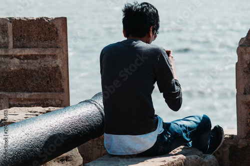 Canvas Print Man taking photograph of his legs while sitting on the wall of fort in Diu, Indi