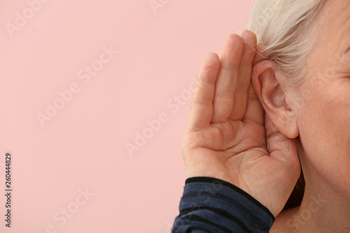 Mature woman with hearing problem on color background, closeup photo