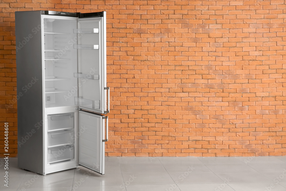 Open empty fridge near brick wall Open empty fridge near brick wall