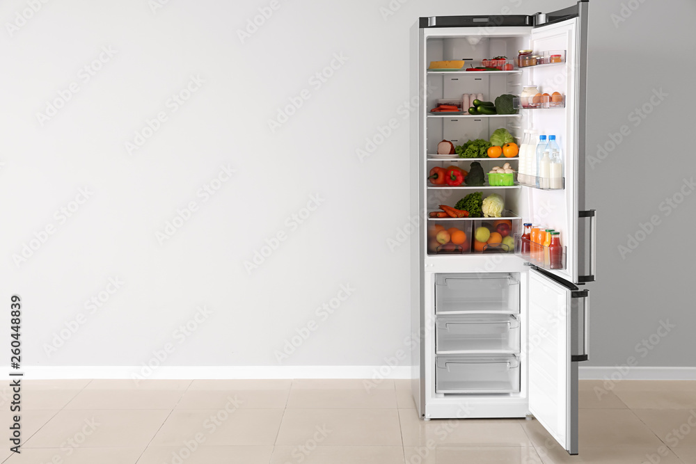 Open fridge full of food near white wall Open fridge full of food near white wall
