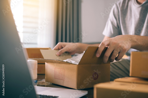 Asian entrepreneur teenager is opening a cardboard box in order to put the product that the customer ordered into the box to deliver the product. © wutzkoh