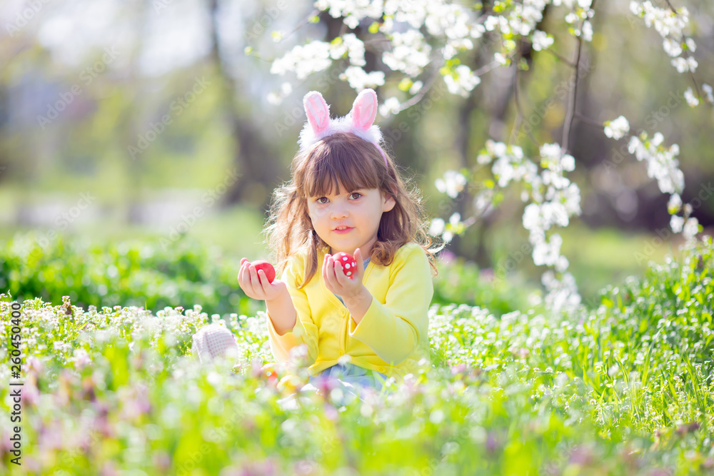 Cute little girl with curly hair wearing bunny ears and summer dress having fun during Easter egg hunt relaxing in the garden Cute little girl with curly hair wearing bunny ears and summer dress having fun during Easter egg hunt relaxing in the garden