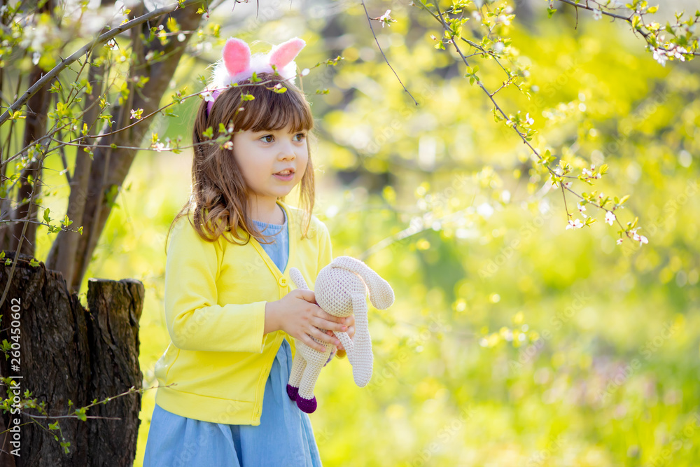 Adorable little funny bunny girl holding rabbit toy in the spring blossom garden Adorable little funny bunny girl holding rabbit toy in the spring blossom garden