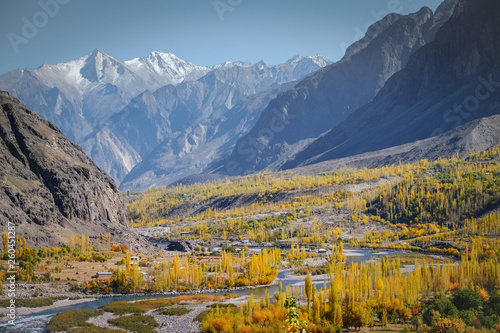 Landscape view of river flowing through forest in Gupis with mountain range in the background. Ghizer in autumn. Gilgit Baltistan, Pakistan.