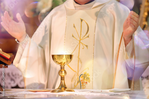 Fototapeta Chalice at the altar with rays of light and Priest celebrate mass