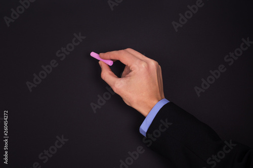 Man hand in suit holds chalk on background of black chalkboard