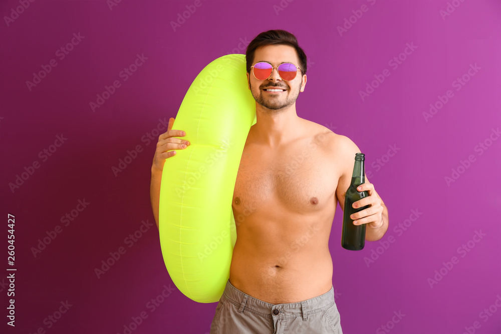 Handsome man with inflatable ring and beer on color background