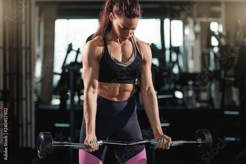Muscular Caucasian woman with ponytail and dressed in sportswear lifting barbells in gym. Earn your body.