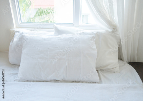White sheets, blanket and pillows on the cozy bed with a window at the back. Bedding concept.