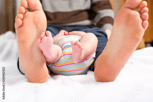 Closeup of huge feet of father and little newborn baby. Big feet of adult and tiny legs of child. Happy parenthood, carefree childhood, family, love, tenderness