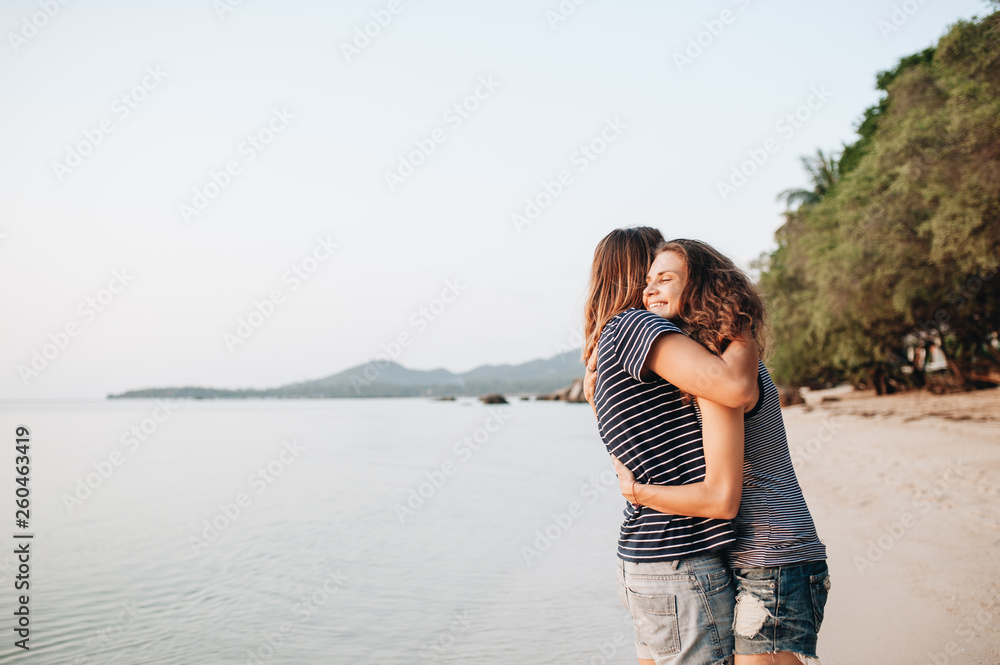 Two smiling friends hugging each other on the beach