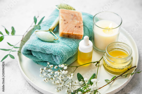 Natural organic skincare cosmetic products tray with natural soap, balm, oil, jade roller, candle and flowers, natural green skincare and spa products