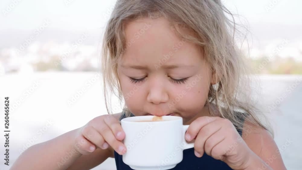 Portrait of little blonde girl is drinking hot chocolate from the white cup. Slow motion. Portrait of little blonde girl is drinking hot chocolate from the white cup. Slow motion.