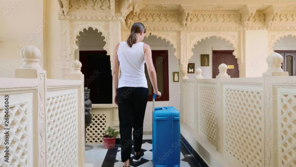 Woman is rolling suitcase in a hotel to check in her room. Back view. Slow motion. Woman is rolling suitcase in a hotel to check in her room. Back view. Slow motion.