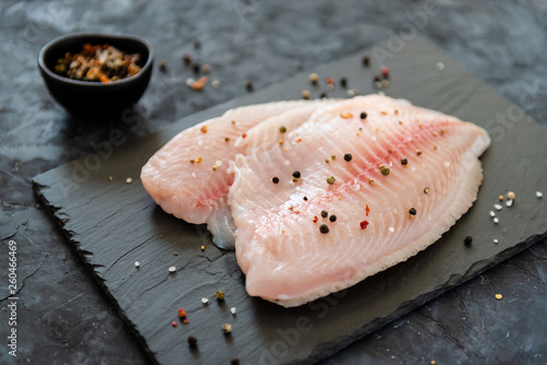 Fotografie Fresh tilapia fillet ready to be cooked, black wooden background