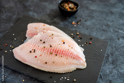 fresh fish fillet with ingredients for cooking on stone plate on dark background. Copy space