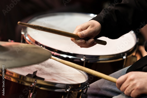 The hands of a man playing a drum set in dark colors