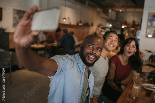 Smiling friends taking selfies together in a bar