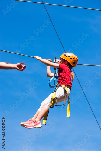 Little brave caucasian girl using a zip line. An indefinited man lend a helping hand.