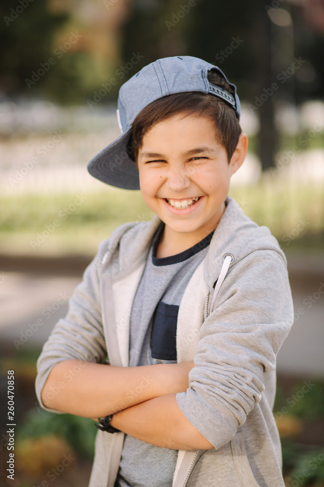 Stylish little school boy in blue cap posing outside for photo. Boy walking in the city in sping summer weather Stylish little school boy in blue cap posing outside for photo. Boy walking in the city in sping summer weather