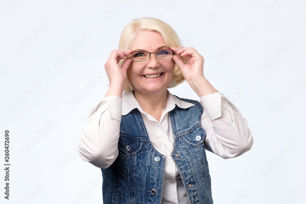 Senior woman adjusting glasses and smiling at you