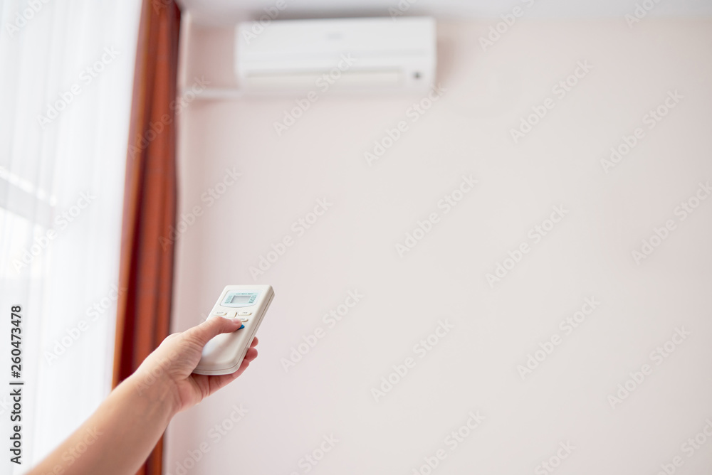 Fototapeta premium Woman hand with remote control operating air conditioner inside the room, copy space