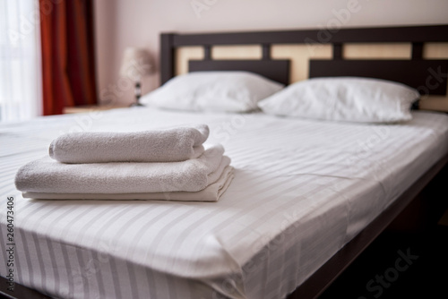 Stack of white clean bath towels on bed sheet in modern hotel bedroom interior, copy space