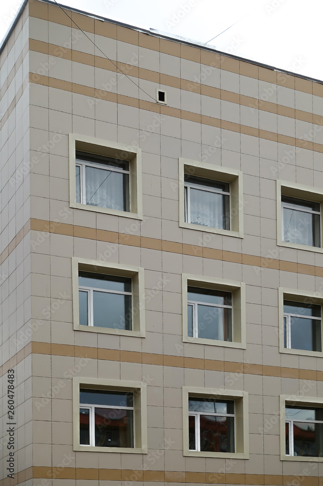 The facade of a multi-storey clinical building. The walls with many windows are finished with plastic.