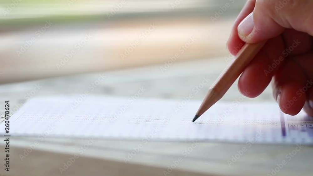 Exam test school or university concept : Hand student holding pencil writing standardized answer multiple carbon paper form with gray black answers sheet bubbled doing final assessment in classroom